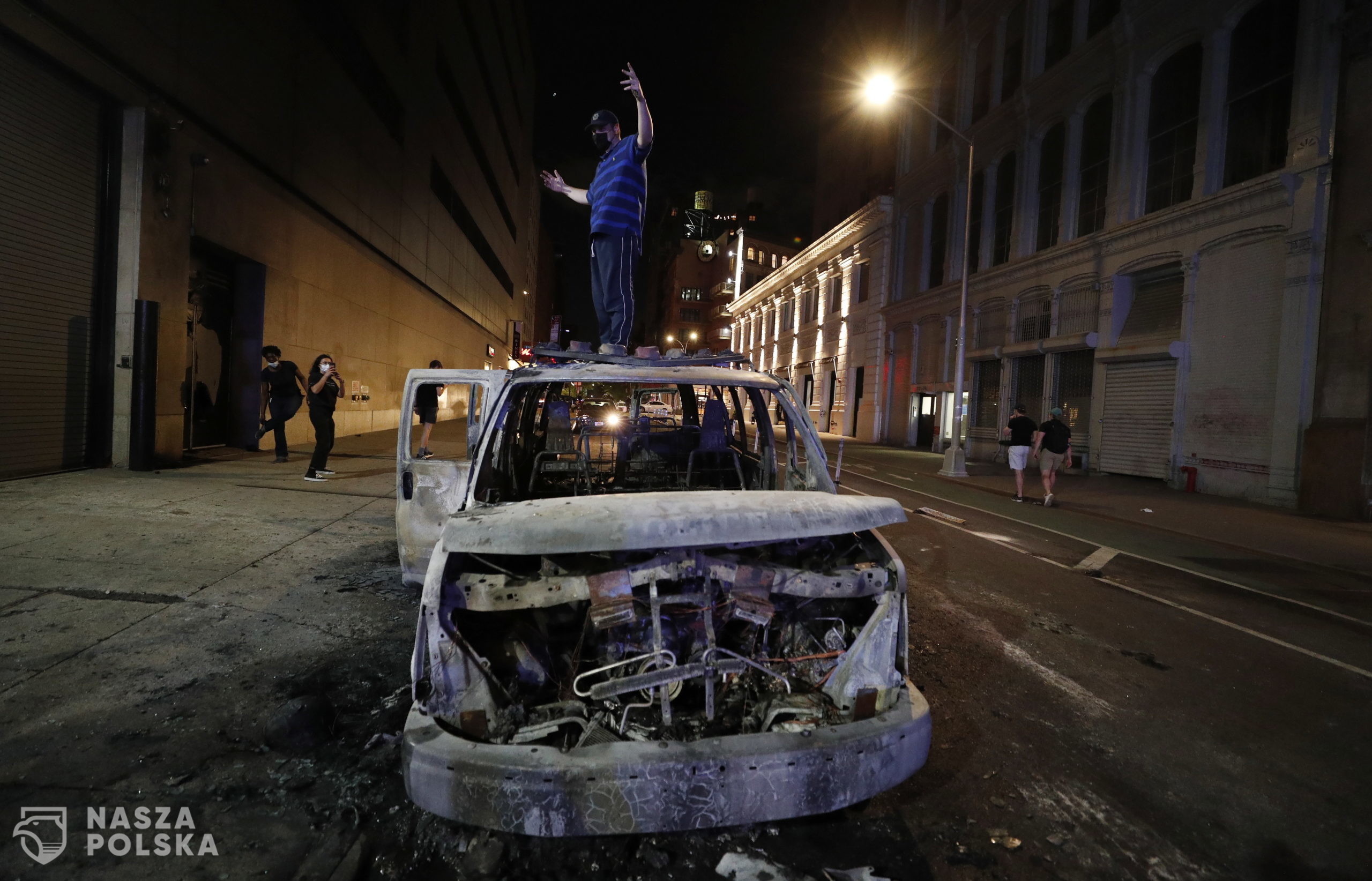 epa08455449 A protester stands on a burned out New York City Police Department vehicle a protesters demostrate about the arrest of George Floyd, who later died in police custody, in New York , New York, USA, 30 May 2020. A bystander's video posted online on 25 May, appeared to show George Floyd, 46, pleading with arresting officers that he couldn't breathe as an officer knelt on his neck. The unarmed black man later died in police custody.  EPA/JUSTIN LANE 
Dostawca: PAP/EPA.