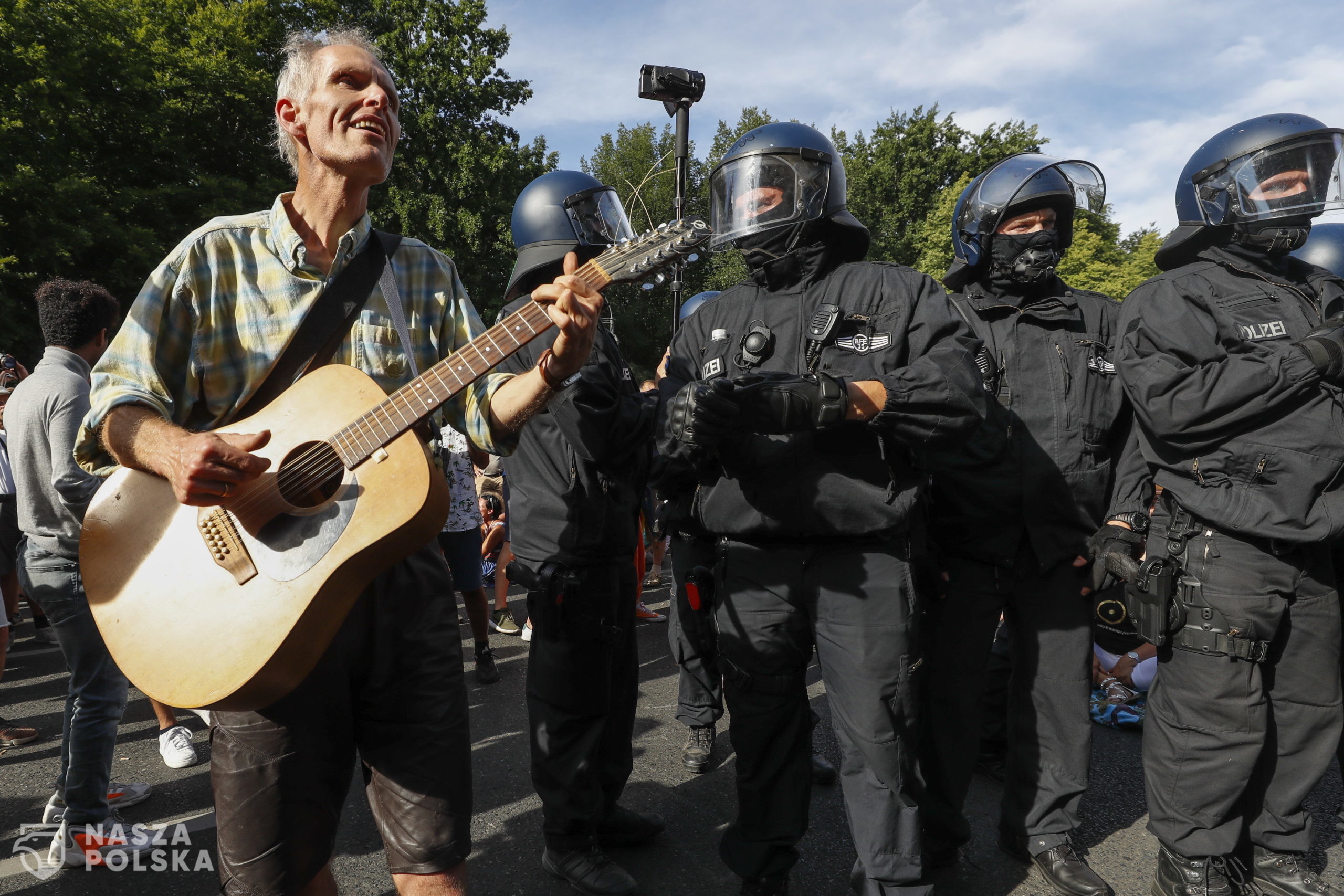 epa08579074 A demonstrator plays on a guitar in front of policemen during a protest against coronavirus pandemic regulations in Berlin, Germany, 01 August 2020. An alliance of right wing groups have called to a democratic resistance demonstration for the first weekend in August. The nationwide rally 'Day of Freedom' will take place 01 August as a protest against the measures imposed by the Government in relation to the coronavirus pandemic. The events are organized by groups of various motives, right wing activists, conspiracy theory believers and more.  EPA/FELIPE TRUEBA 
Dostawca: PAP/EPA.