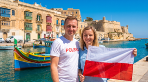 Polacy na Malcie - para z polską flagą przy tradycyjnej łodzi luzzu w porcie pod bastionami Valletty, zdjęcie wygenerowane AI