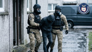 Funkcjonariusze ABW w maskach wyprowadzają z budynku zatrzymanego mężczyznę z zakrytą twarzą