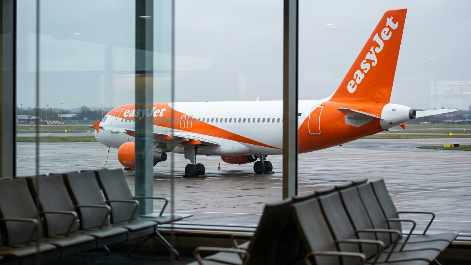 Puste fotele w poczekalni przy bramce i samolot EasyJet zaparkowany na mokrej płycie lotniska