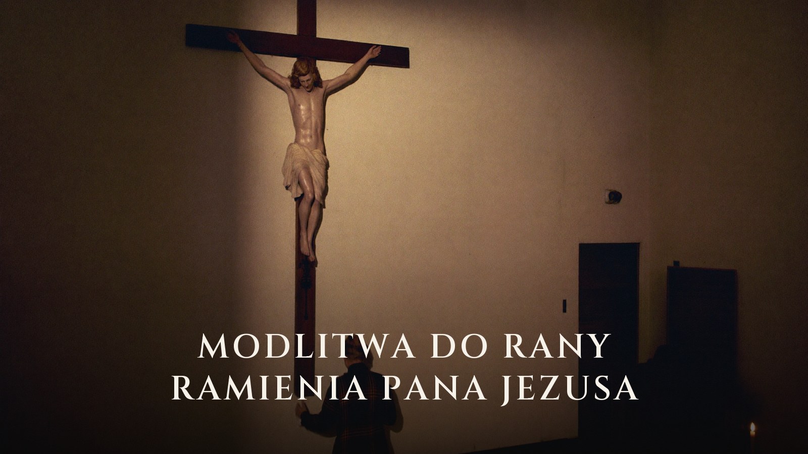 Mężczyzna stoi ze świecą u stóp dużego krucyfiksu w mroku kościoła