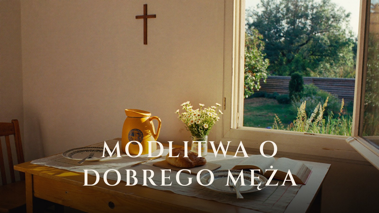 Stół nakryty dla dwojga przy otwartym oknie, chleb, dzbanek i stokrotki, na ścianie drewniany krzyż