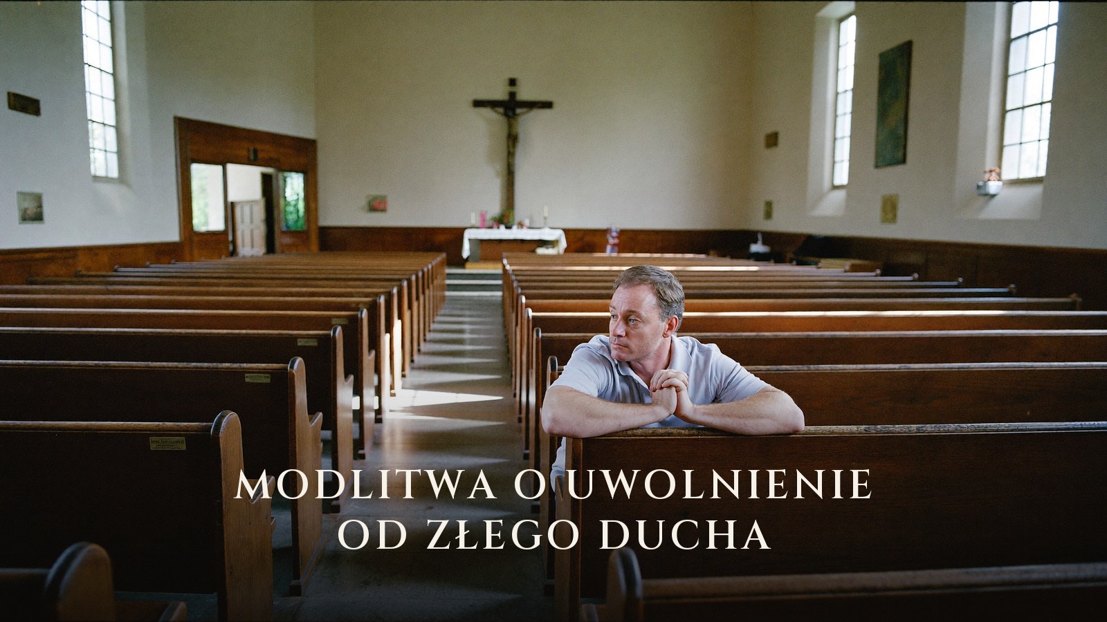 Mężczyzna modli się samotnie w ławce pustego kościoła, nad ołtarzem widoczny krzyż