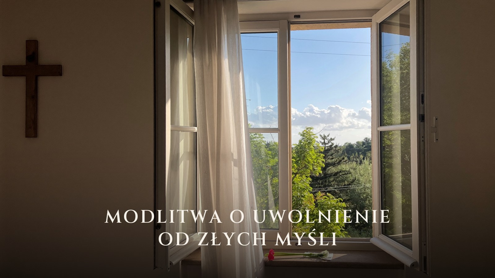Otwarte okno z firanką i letnią zielenią, obok na ścianie drewniany krzyż