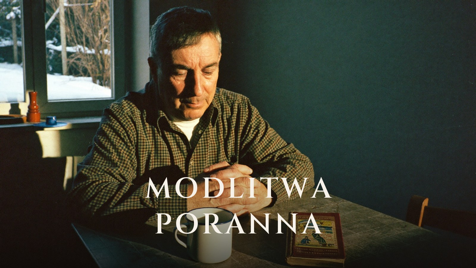 Starszy mężczyzna ze złożonymi dłońmi modli się przy kuchennym stole w zimowym porannym słońcu