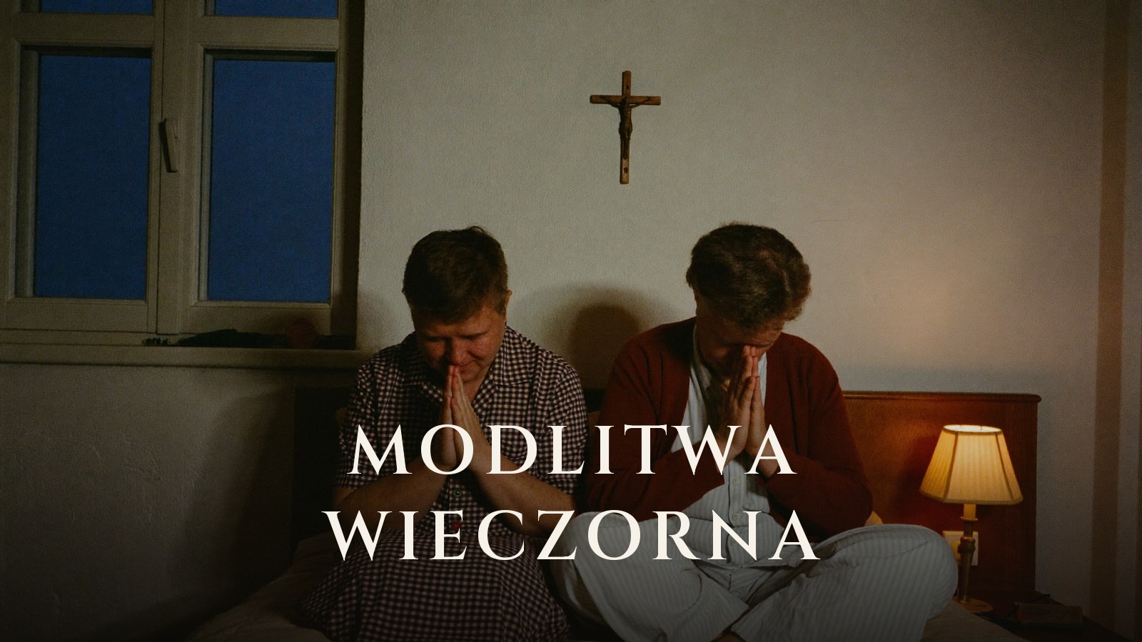 Starsze małżeństwo modli się wieczorem na brzegu łóżka pod krucyfiksem