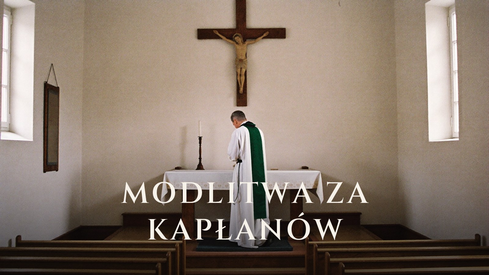Kapłan w albie i zielonej stule stoi pochylony przy ołtarzu pustego kościoła, powyżej krucyfiks