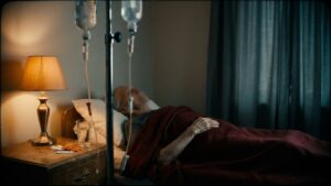 Opieka paliatywna w hospicjum domowym: chory leży w łóżku przy stojaku z dwiema kroplówkami, obok lampka i leki