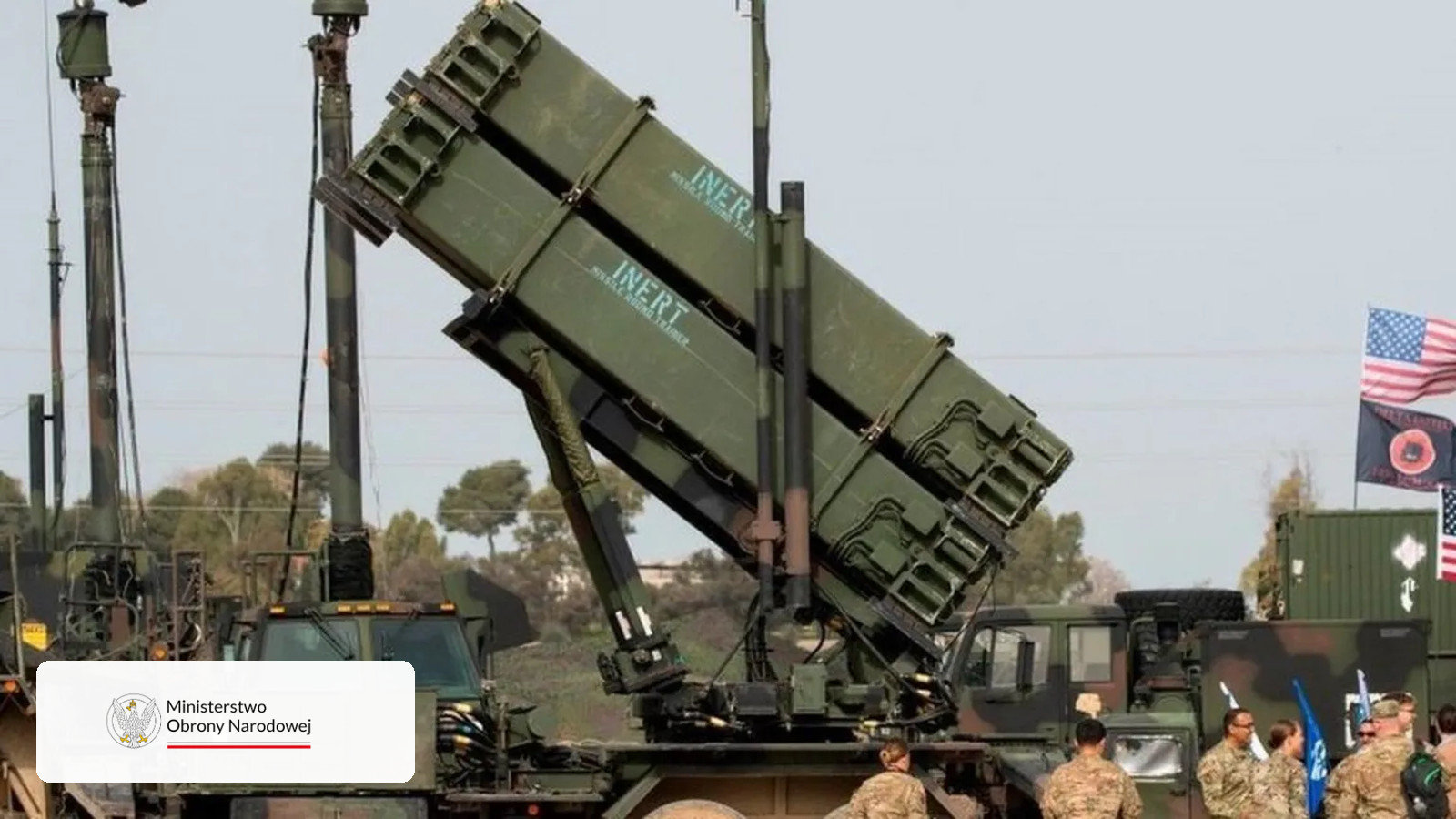 Wyrzutnia systemu Patriot z uniesionymi kontenerami startowymi, obok żołnierze i flagi Stanów Zjednoczonych