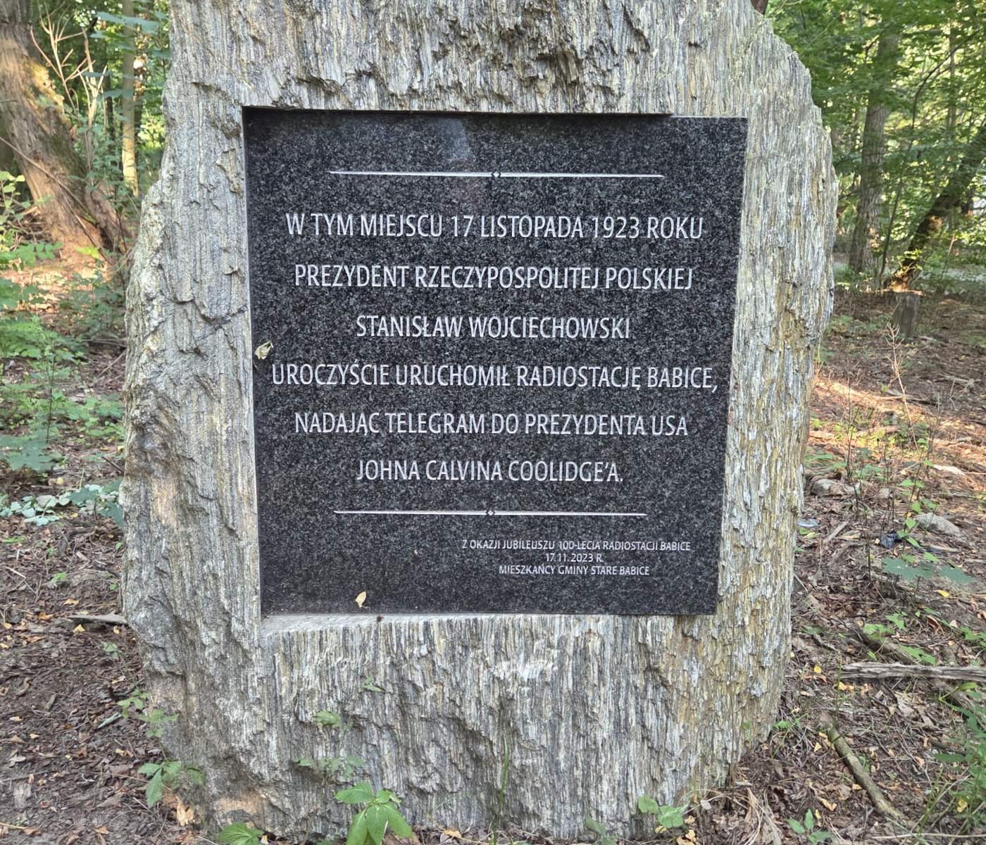 Kamień z granitową tablicą upamiętniającą uruchomienie radiostacji Babice, ustawiony wśród drzew