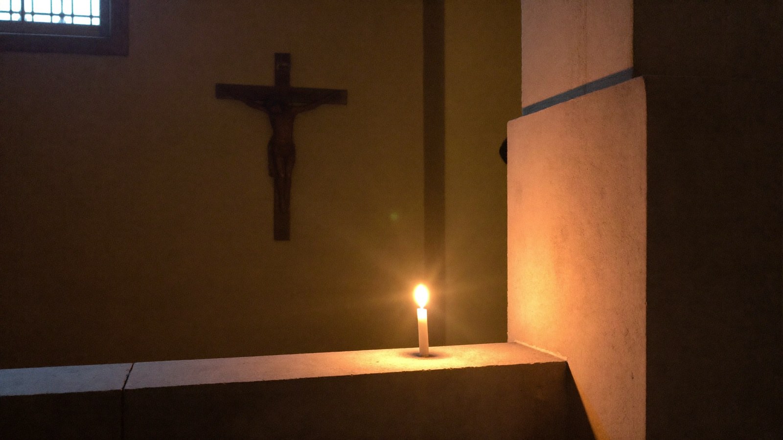 Zapalona świeca rozjaśnia wnętrze kościoła pod krzyżem