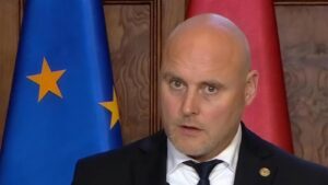 Premier Łotwy Andris Kulbergs na konferencji o wojnie hybrydowej Rosji, w tle flagi Unii Europejskiej i Łotwy