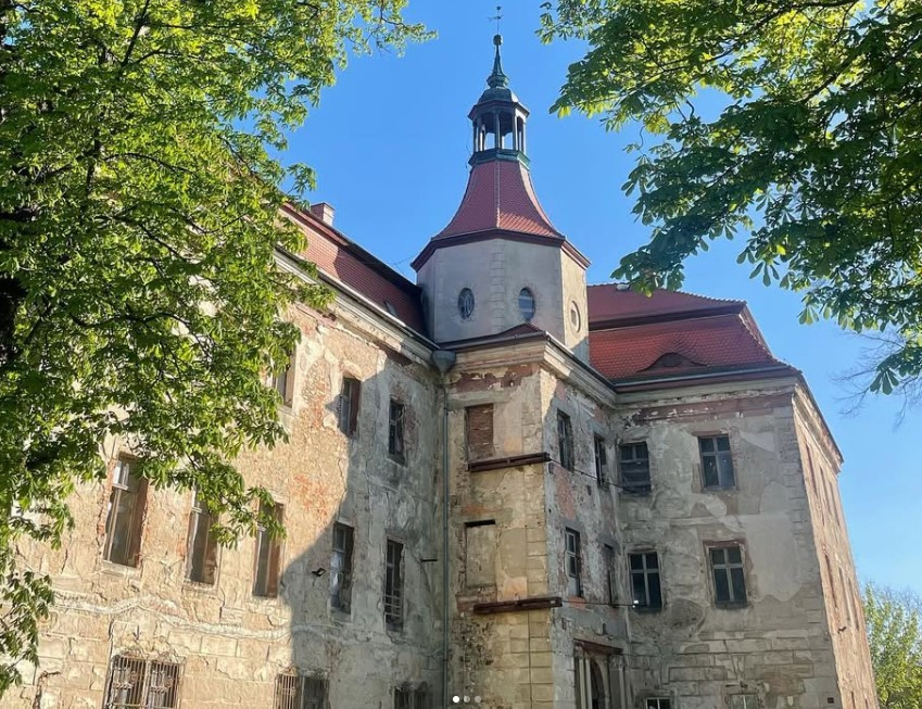 Wieża zamku w Domanicach z nowym czerwonym dachem widziana od strony parku w słoneczny dzień