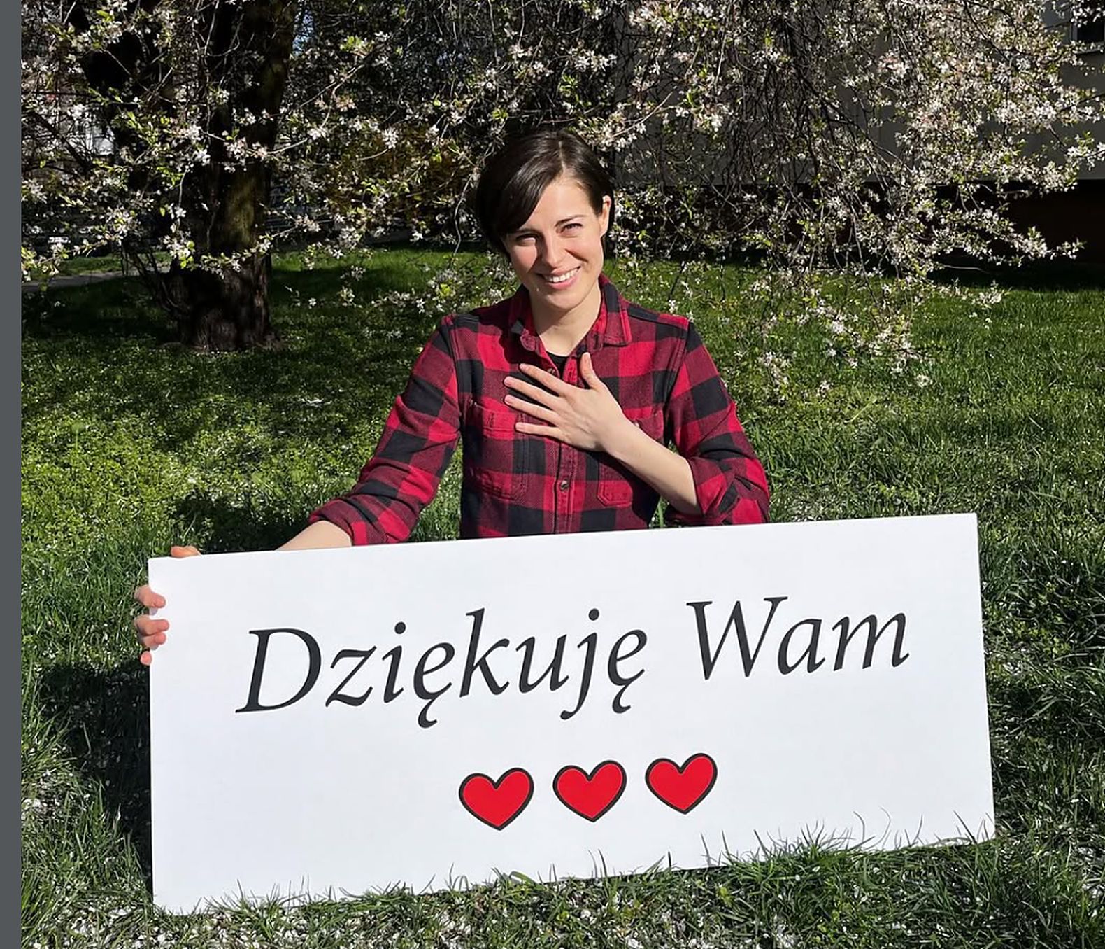 Aleksandra Wierzbicka z tabliczką Dziękuję Wam i trzema czerwonymi sercami w kwitnącym ogrodzie