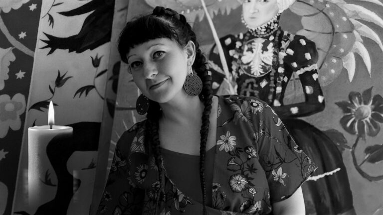 Anna Kaszuba-Dębska przed muralem z postacią polskiej królowej, obok niej pali się świeca