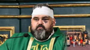 Ksiądz Adrian z Jarosławia z opatrunkiem na głowie i podbitym okiem przy ambonie, obok płonące znicze