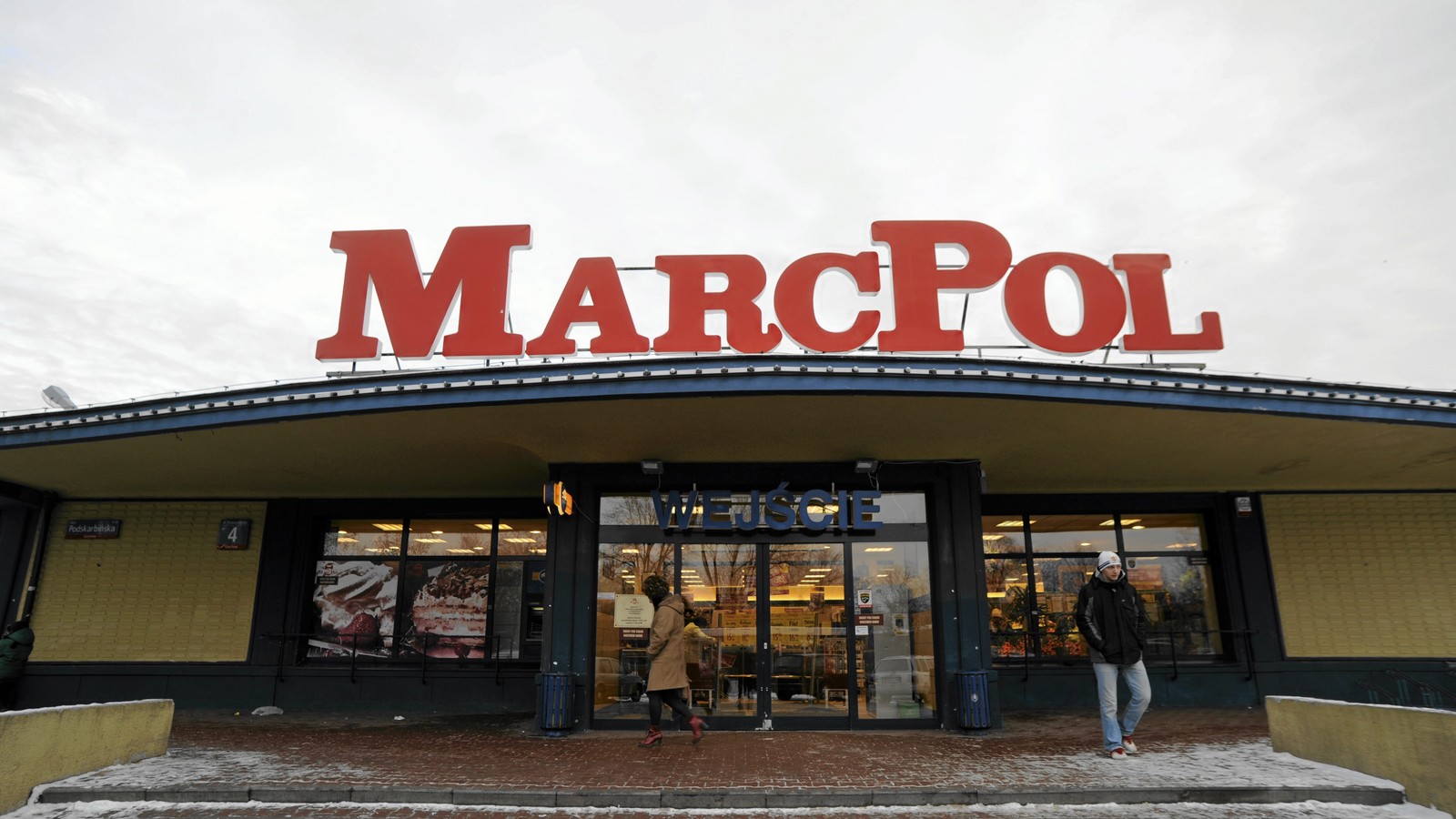 Klienci przy wejściu do supermarketu MarcPol z czerwonym szyldem nad wejściem, zdjęcie archiwalne