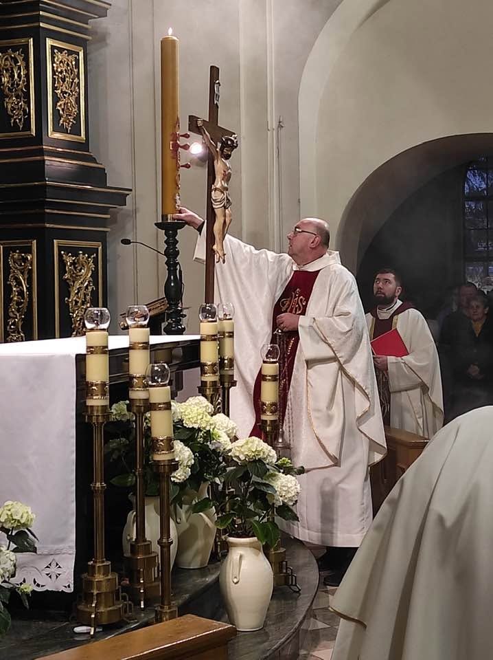 Ksiądz Marek Pieńkowski w białym ornacie przy zapalonym paschale i krzyżu podczas liturgii w kościele