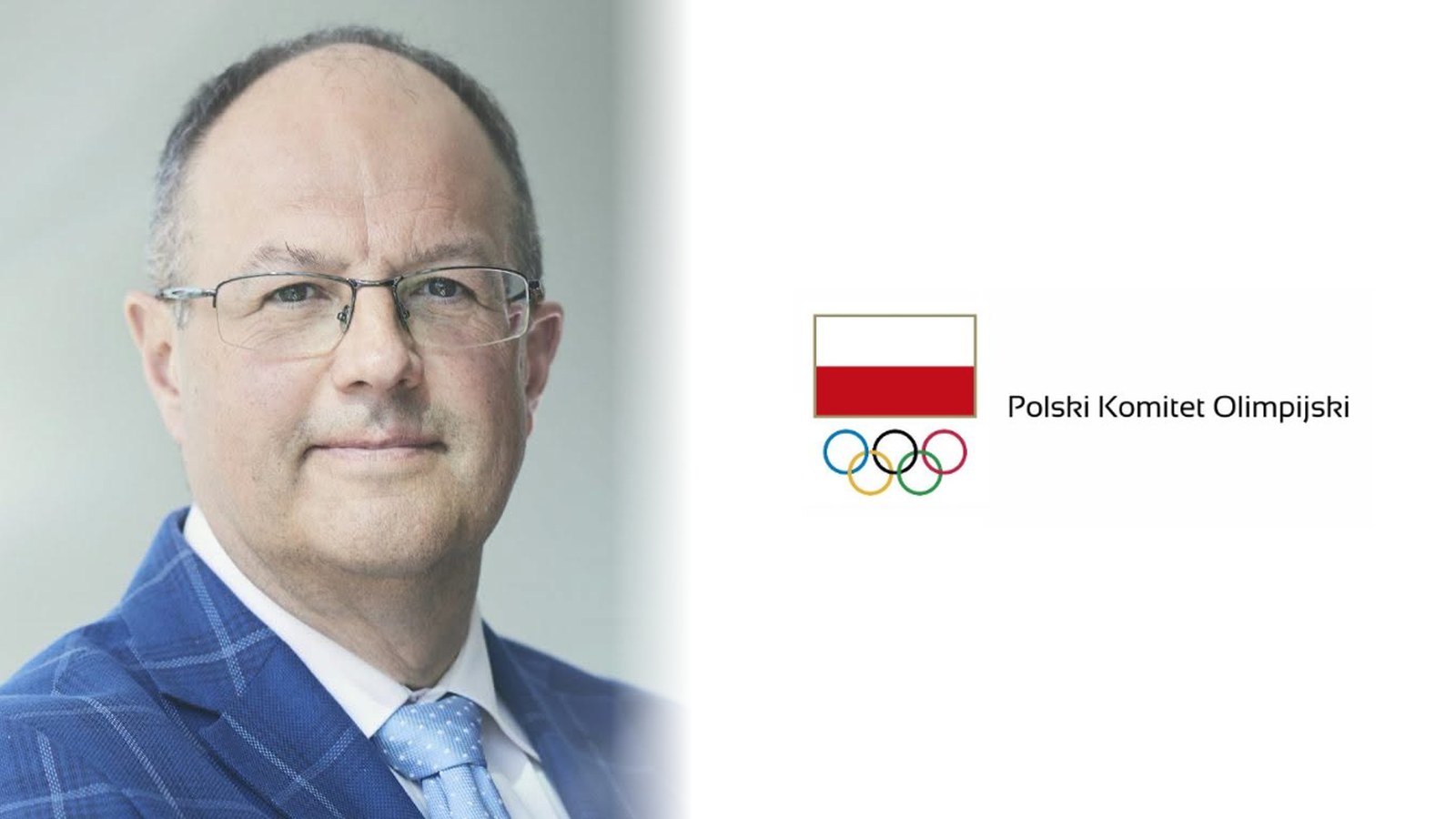 Marian Kmita w granatowej marynarce w kratę, obok logo Polskiego Komitetu Olimpijskiego