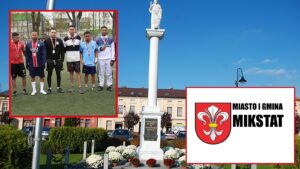 Rynek w Mikstacie z kolumną Serca Jezusowego, obok grupa cudzoziemców pracujących w gminie i herb gminy