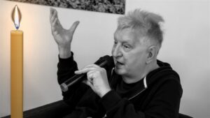 Ryszard Lenczewski z mikrofonem podczas spotkania, obok wysoka zapalona świeca, zdjęcie czarno-białe