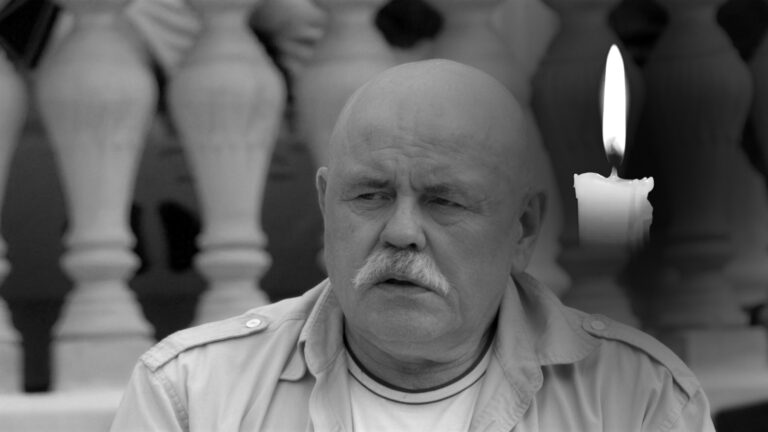 Stanisław Szelc w jasnej koszuli siedzi przy kamiennej balustradzie, obok pali się świeca, kadr czarno-biały