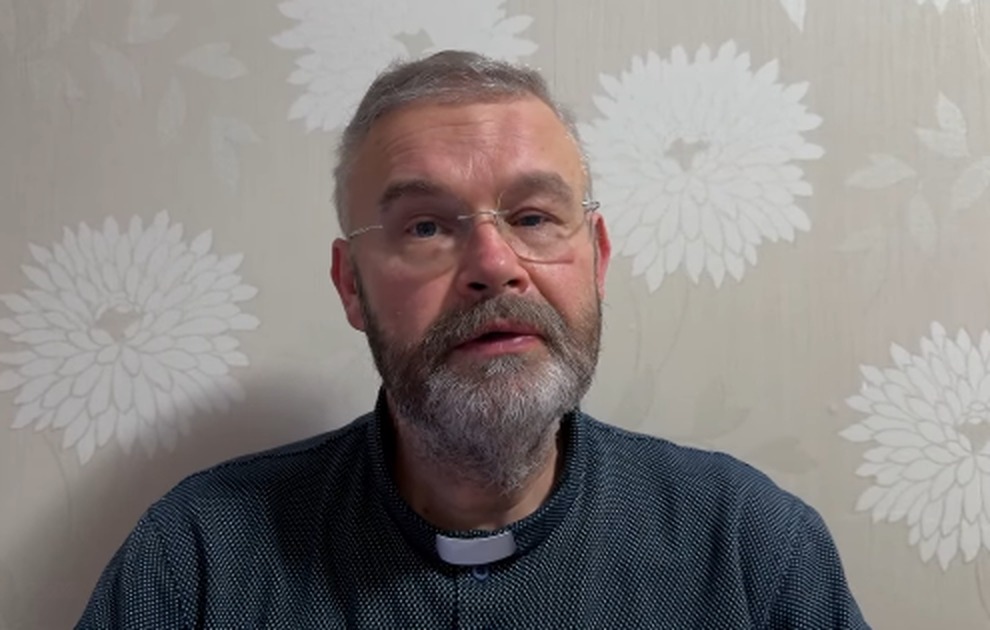 Ksiądz Wojciech Drab w koloratce i okularach podczas nagrywania internetowej medytacji biblijnej