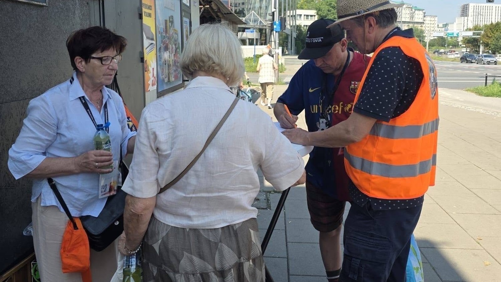 Warszawianka podpisuje wniosek o referendum przy stoliku wolontariuszy w pomarańczowych kamizelkach