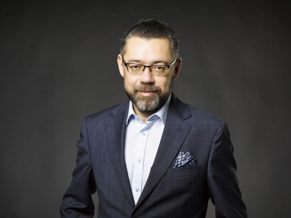 Adwokat Krzysztof Dmowski w ciemnej marynarce i okularach na szarym tle