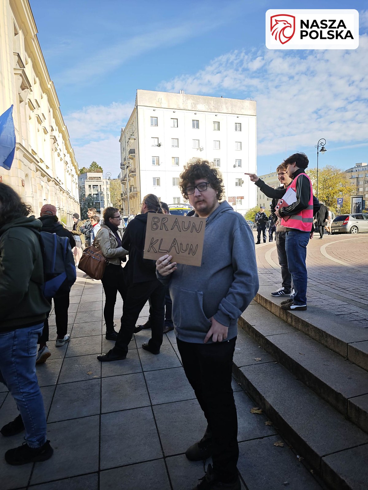 Uczestnik manifestacji z kartonowym transparentem Braun klaun przy pomniku Kopernika w Warszawie