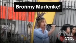 Kobieta w błękitnej koszuli przemawia przez mikrofon na proteście w obronie dzików przed warszawskim ratuszem