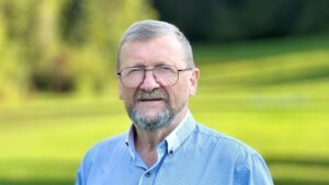Dr inż. Jacek Pulikowski w okularach i niebieskiej koszuli na tle zielonego parku