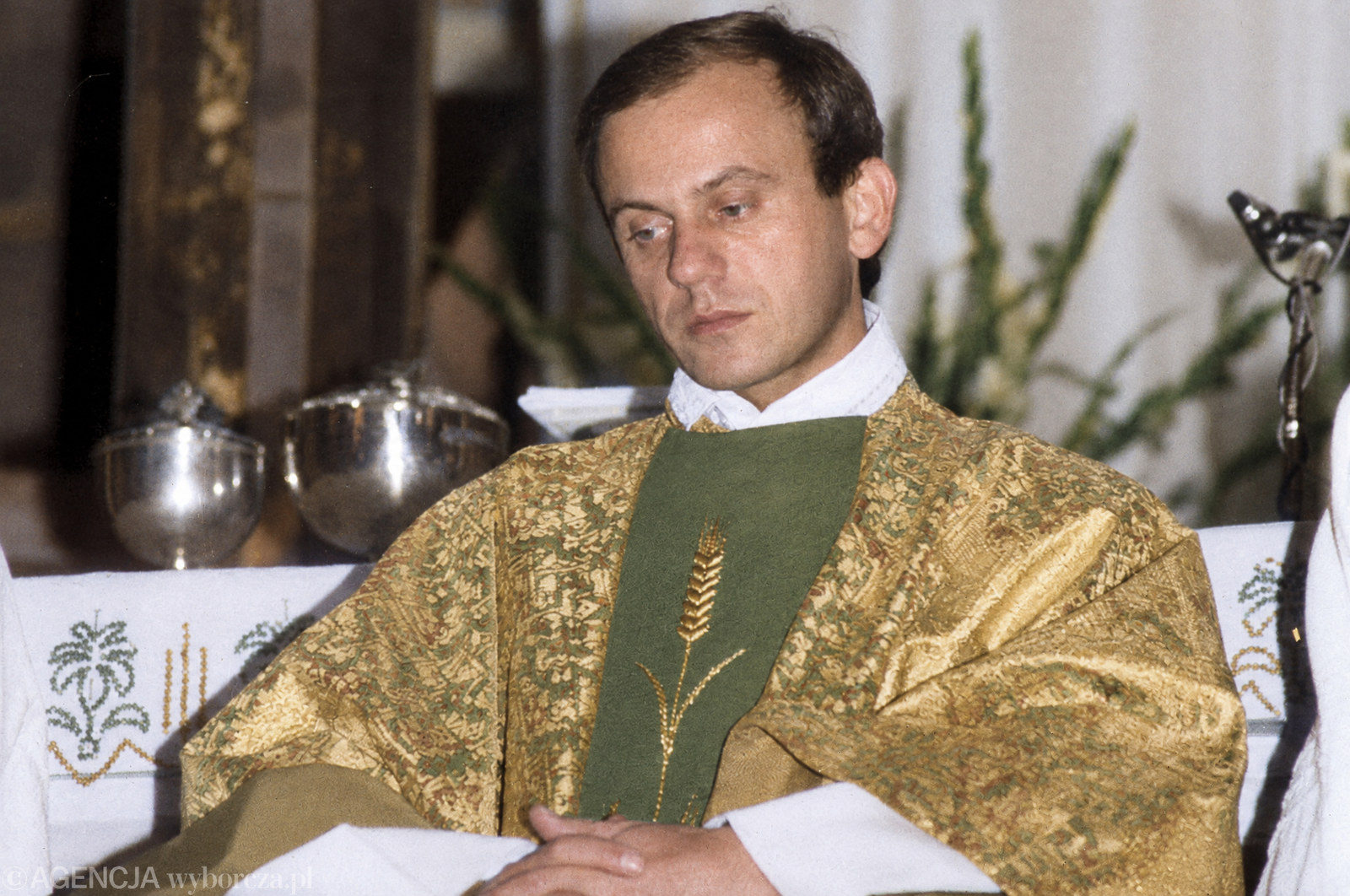 Ks. Jerzy Popiełuszko w złoto-zielonym ornacie z motywem kłosa siedzi przy ołtarzu w czasie Mszy