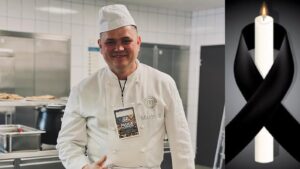 Mariusz Komenda w bieli kucharskiej z plakietką MasterChefa, obok świeca z czarną wstążką