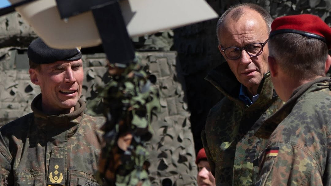 Friedrich Merz w mundurze polowym rozmawia z oficerami Bundeswehry przy pojeździe okrytym siatką maskującą