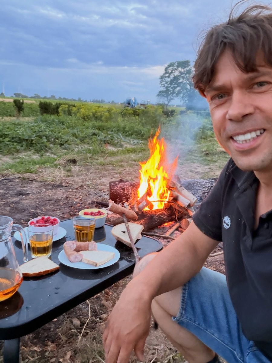 Michał Kołodziejczak przy ognisku na skraju pola, w tle deszczownia i ciągnik nawadniające uprawy