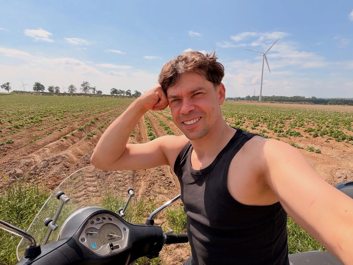 Michał Kołodziejczak na skuterze przy świeżo obsadzonym polu ziemniaków, w tle turbina wiatrowa
