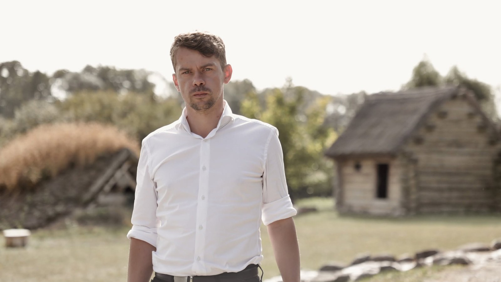 Michał Kołodziejczak, lider Agrounii, w białej koszuli na tle drewnianej chaty i ziemianki
