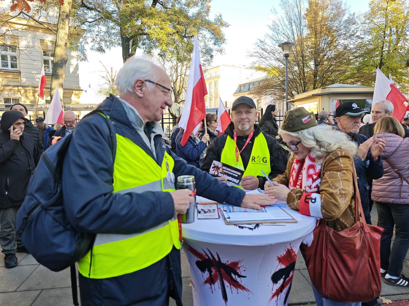 Wolontariusze w odblaskowych kamizelkach zbierają podpisy przy stoliku podczas zgromadzenia pod Trybunałem Konstytucyjnym