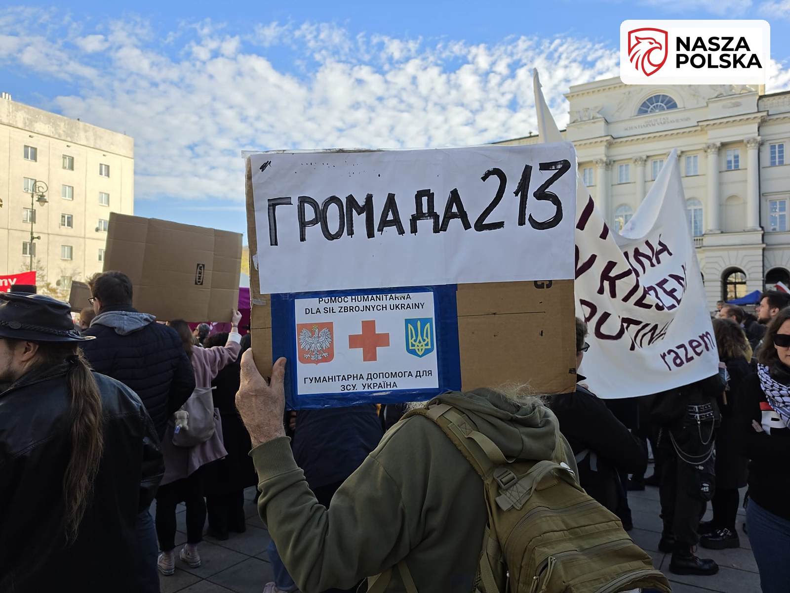 Uczestnik manifestacji z transparentem Hromada 213 i informacją o pomocy humanitarnej dla Ukrainy