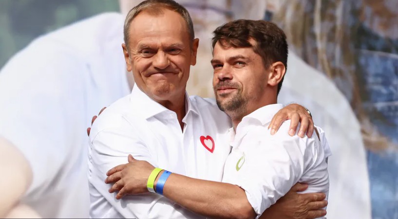 Donald Tusk obejmuje uśmiechniętego Michała Kołodziejczaka na scenie, obaj w białych koszulach