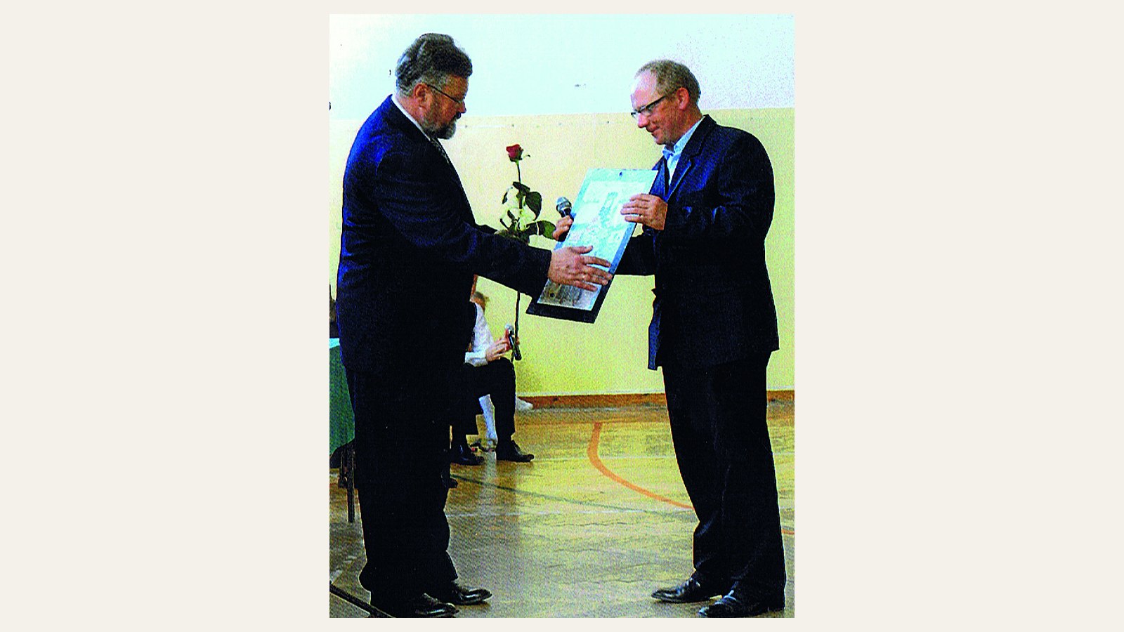 Grzegorz Woś wręcza oprawiony obraz dyrektorowi szkoły w Rogowie, w tle sala gimnastyczna