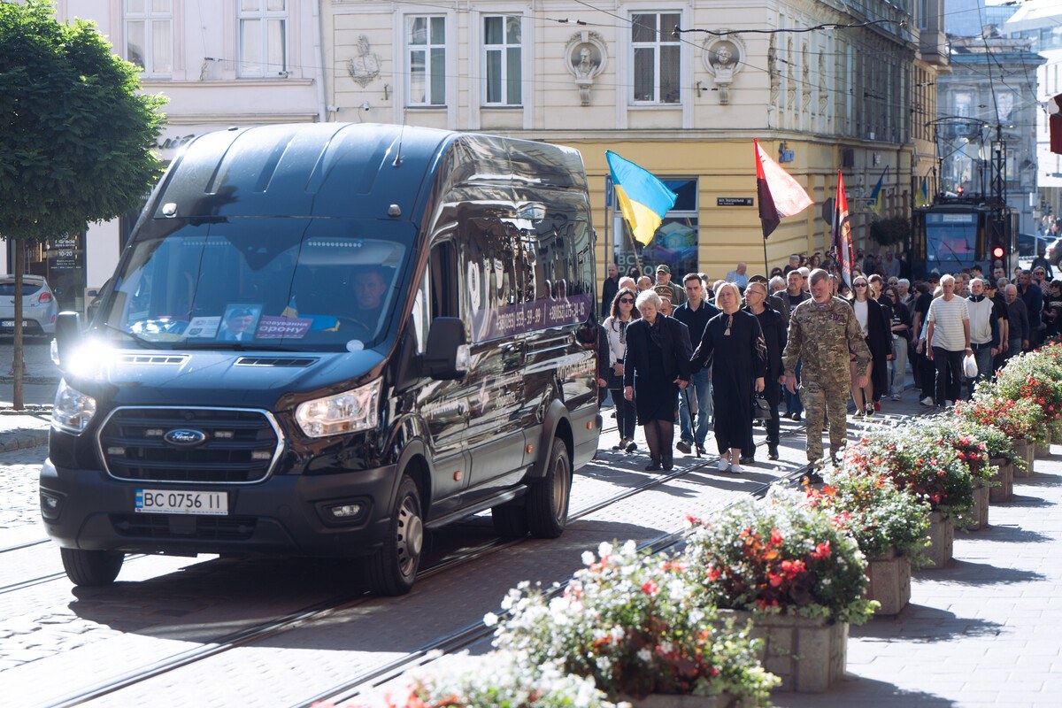 Kondukt żałobny za karawanem na ulicy Lwowa, w tłumie flagi Ukrainy i czerwono-czarne flagi banderowskie